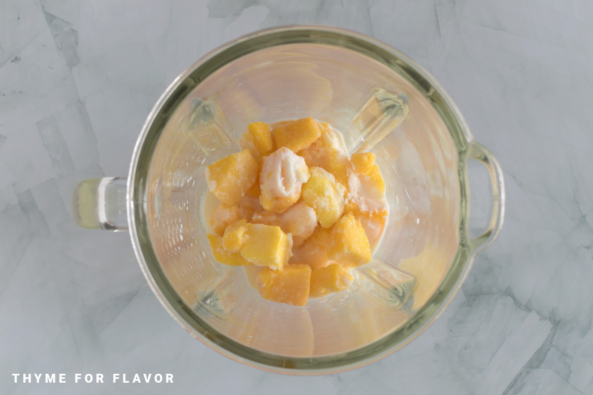 Mango, milk, and maple syrup in a blender before blending.