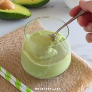 Avocado smoothie in a small round glass with a spoon.