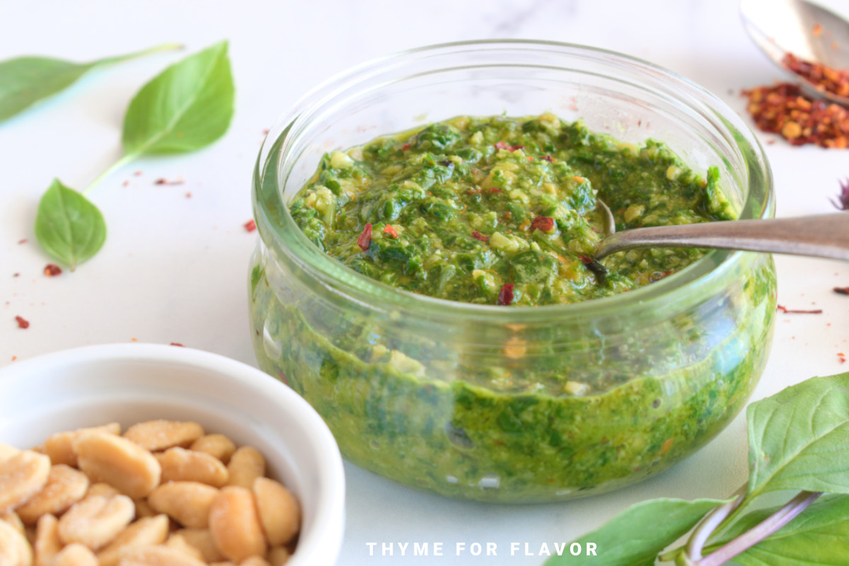 Thai basil pesto in a glass container with a spoon.