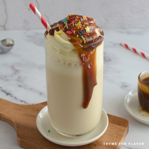 Close up image of a butterscotch milkshake in a glass on a white coaster.
