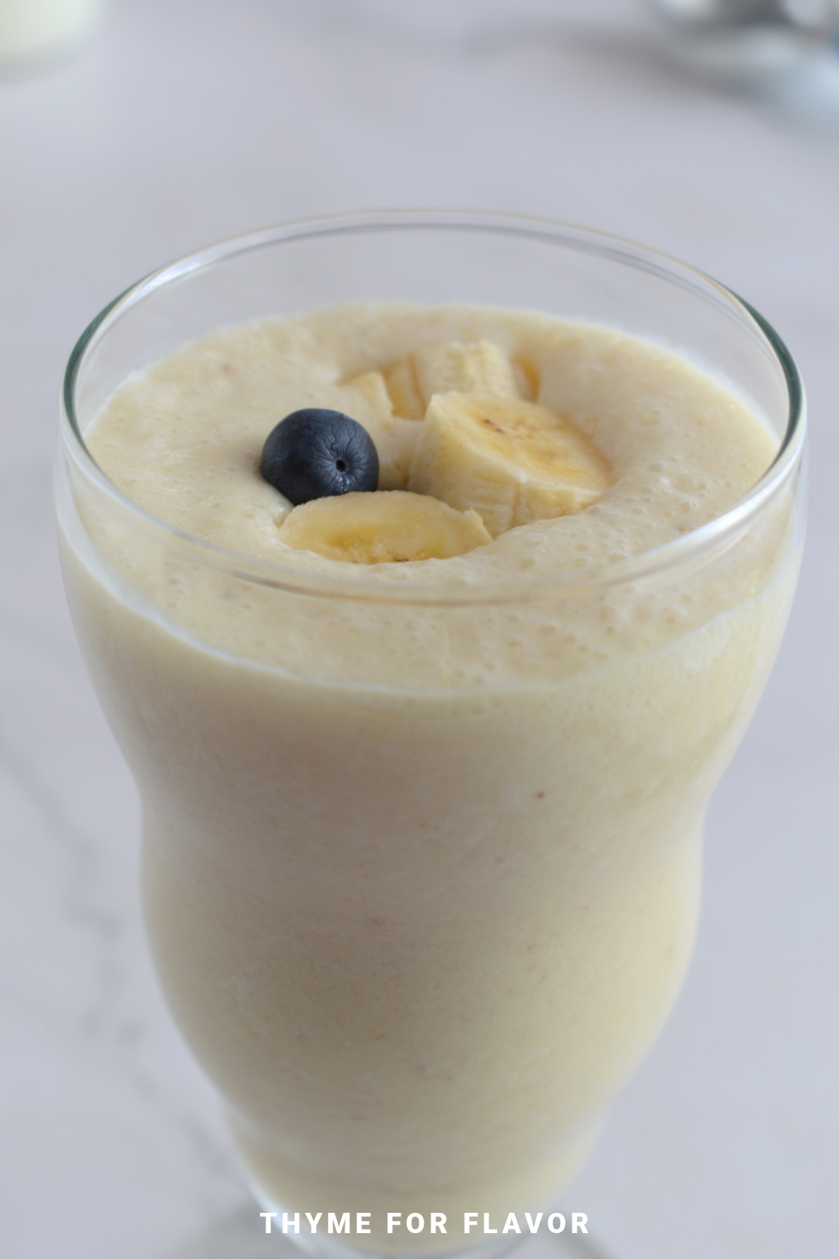 Banana milkshake in a tall glass, with sliced bananas and a blueberry.