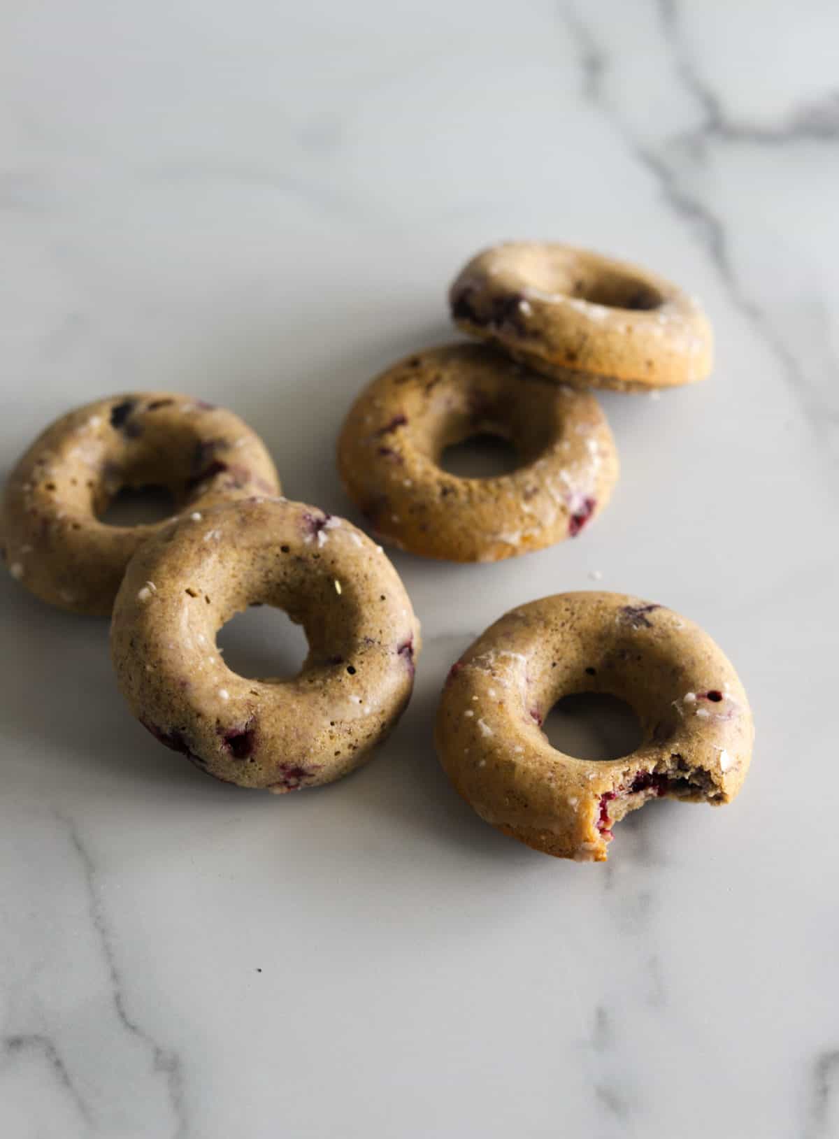 Baked blueberry donuts on a marble benchtop.