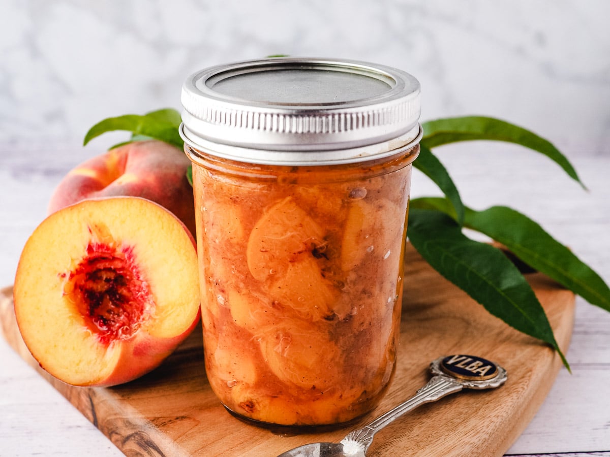 Peach compote in a sealed jar on a wooden board.