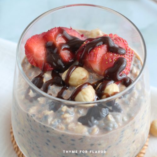 Nutella overnight oats in a glass with fresh strawberries, hazelnuts, and chocolate drizzle.