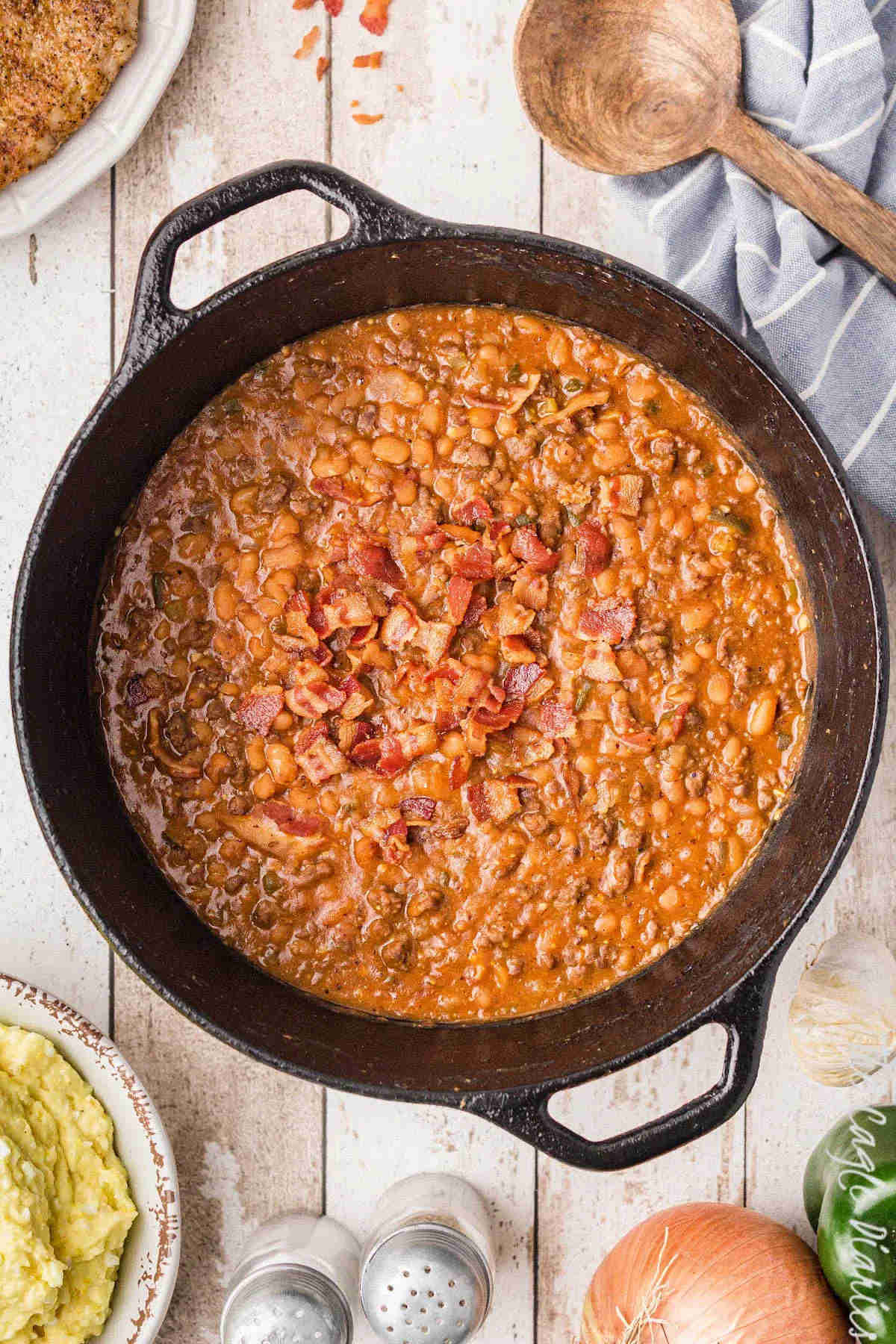 Baked beans in a skillet on a wooden benchtop.