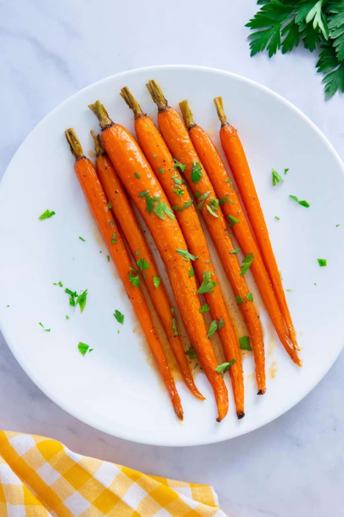 Maple glazed carrots on a round white plate, garnished with parsley leaves.