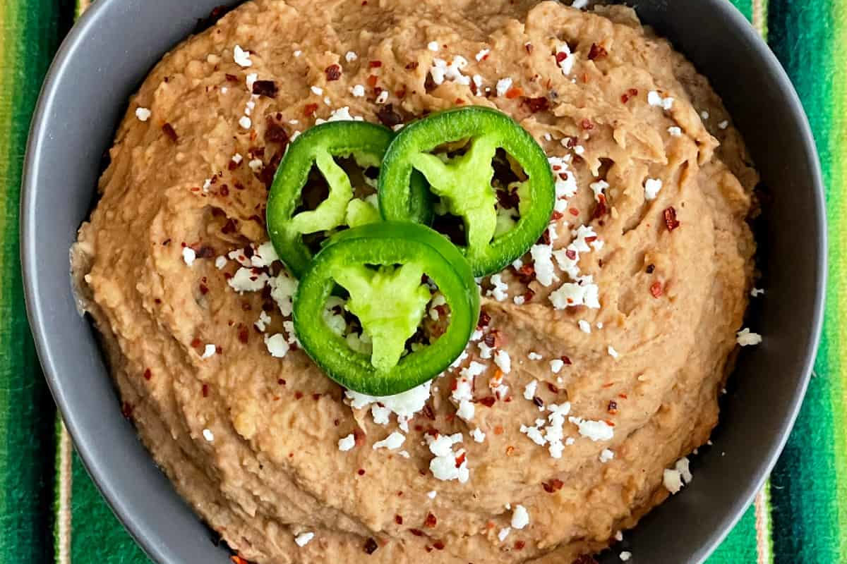 Close up image of refried beans in a black bowl with sliced green chilis on top.