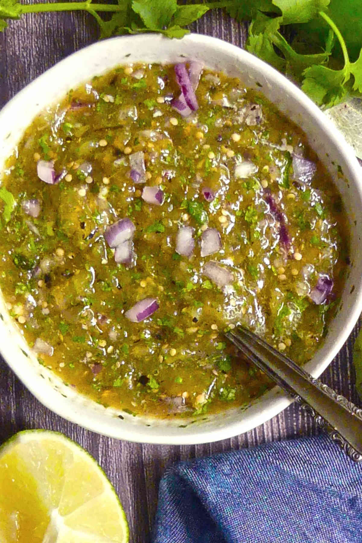 Salsa verde in a white bowl with a spoon.