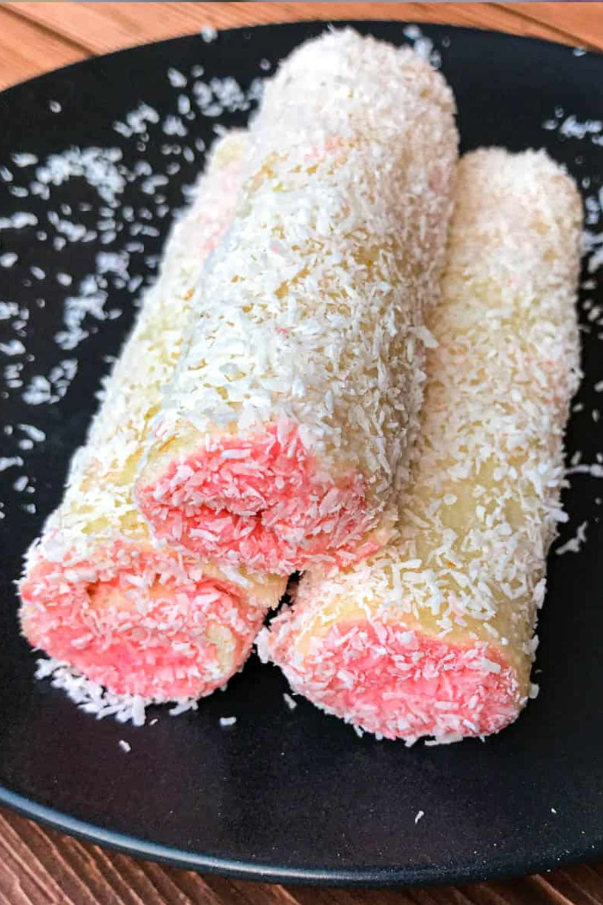 Close up image of strawberry coconut rolls on a black plate.