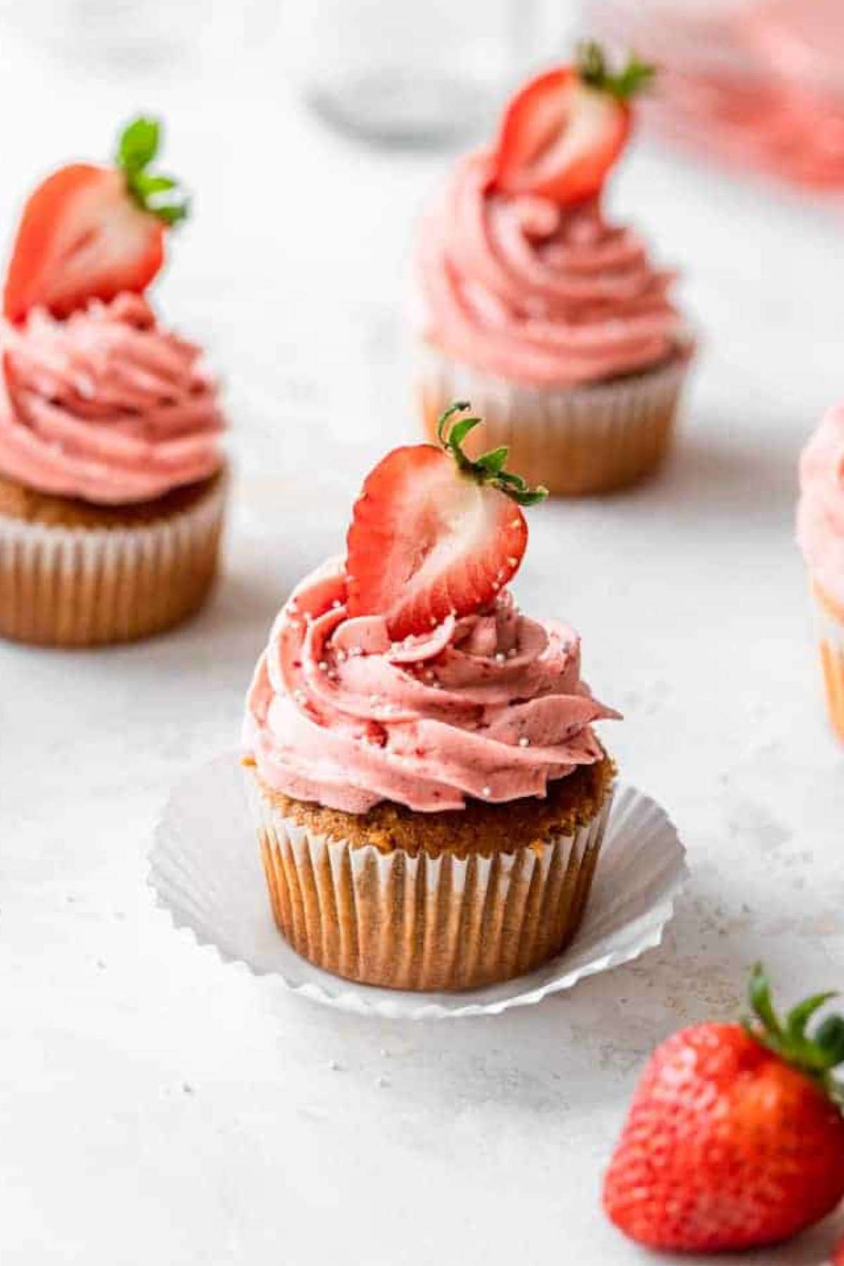 Close up image of strawberry cupcakes in cupcake cases on a benchtop.