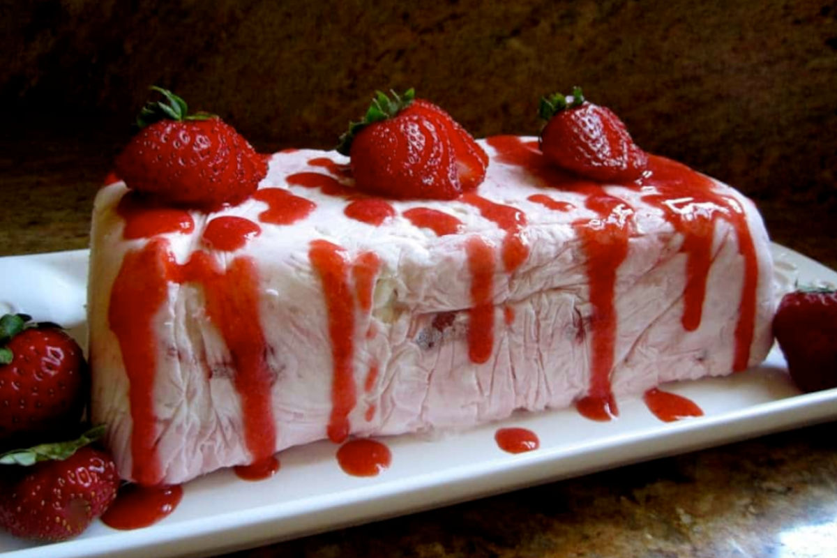Close up image of a frozen strawberry meringue cake on a rectangle plate.