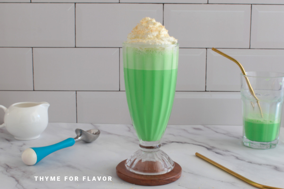 Pandan milkshake in a glass topped with whipped cream and toasted coconut.